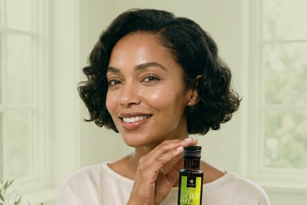 Woman holding 100ml olive oil bottle for skin-care routine. 