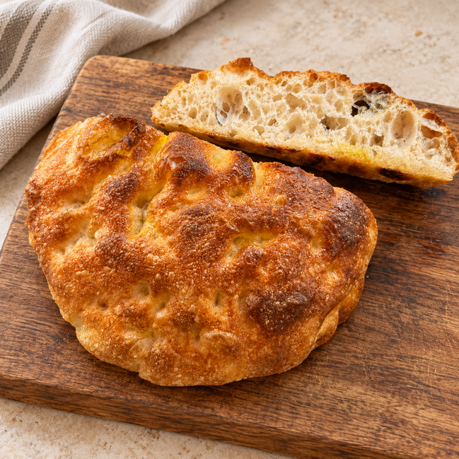 Round handmade ITALOIL olive oil focaccia with a sliced piece showing its airy crumb